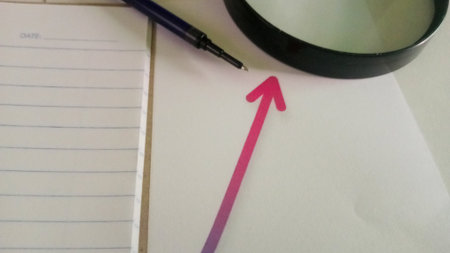 Magnifying glass and pen on a white paper with a red arrowの写真素材