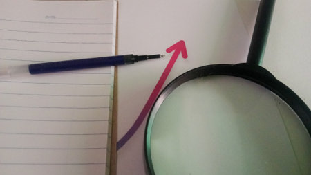 Magnifying glass, pen and notebook with a red arrow pointing upの写真素材