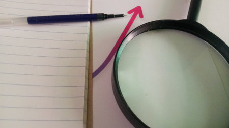 Magnifying glass and pen on a notebook with an arrow going upの写真素材