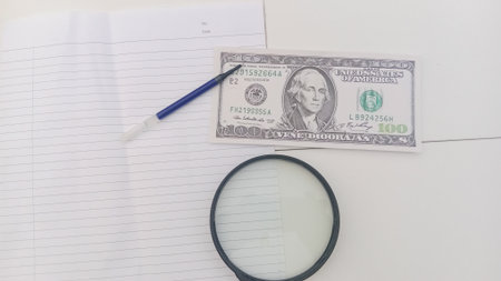 Dollars, magnifying glass and notepad on white background