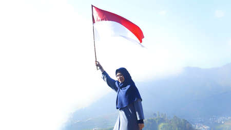 Wonosobo, Indonesia August 17, 2019. Dieng, Muslim girl is waving the flag with a nature view, she is commemorating Indonesia of independence Dayのeditorial素材