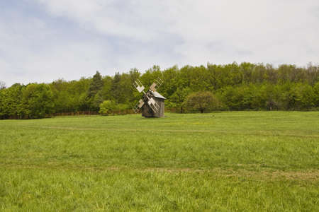 Wooden windmill in green field, forest on background. Recorded in outdoors museum of national architecture in Pirogovo near Kiev in Ukraine.の写真素材