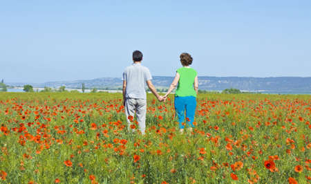 Couple of lovers standing on meadow with poppies shaking hands.の写真素材