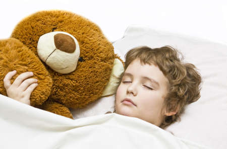 Little boy (European) sleeping in bed with toy bear.
