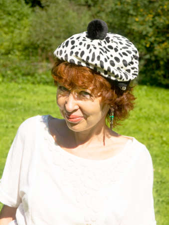 Portrait of European woman with brown hair in white hat with black spots, half body.