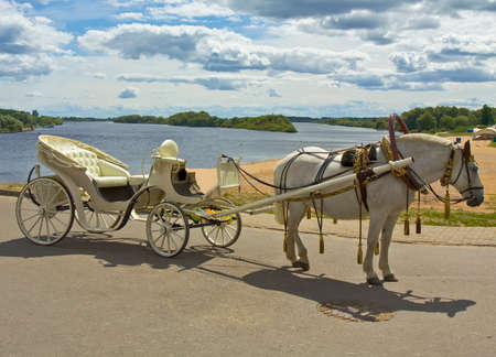 White horse with white carriage on bank of river, in town Great Novgorod, Russia
