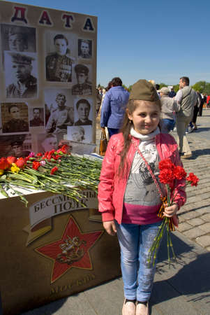 MOSCOW - MAY 9, 2014  Holiday Victory Day devoted to victory in Second World War,  exhibition of photographs of war veterans and little girl with holiday symbols on dress - military field cap, Saint George ribbon and red carnations on the street のeditorial素材