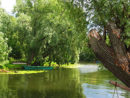 Summer landscape - little river, willow trees on banks and wooden boat. Recorded in town Pereslavl-Zalesskiy, Russia.の写真素材