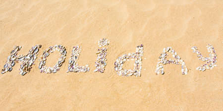 Word "Holiday" made from shells on yellow sand.の写真素材