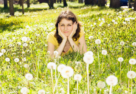 Young woman lays on meadow with white dandelions.の写真素材