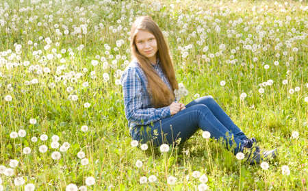 Young beautiful girl, sixteen years, European, long brown hair, sits on meadow with white dandelions.の写真素材