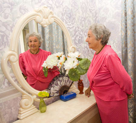 Elderly European woman in bedroom near mirror.の写真素材