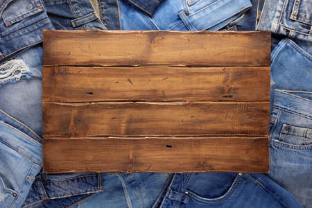 Stack of blue jeans denim and wood name plate. Jeans heap with wooden background textureの写真素材