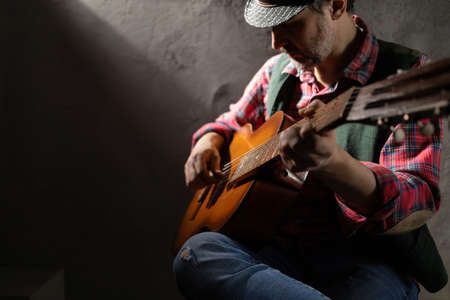 Man playing acoustic guitar. Musician in studio with classic acoustic guitar near wall