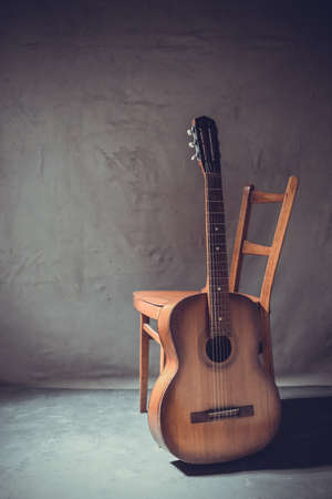 Old acoustic guitar near chair at floor. Music concept in studio with musical instrument near wallの写真素材