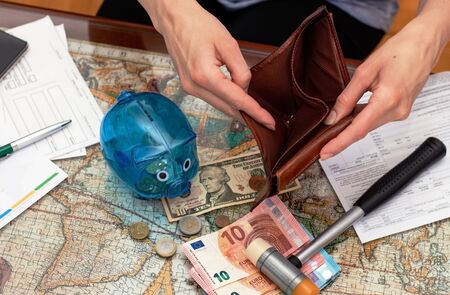 Top view of a piggy bank, hammer, cash in different currencies, unpaid bills and empty wallet in woman hands on the table. Concept of money saving economy for rainy days.の写真素材