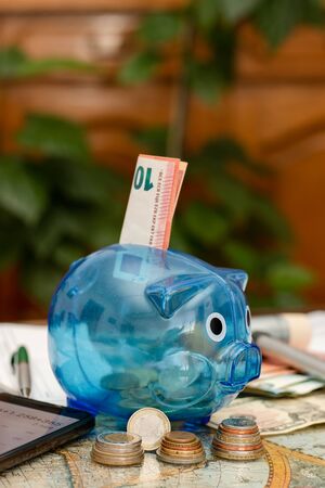 Piggy bank, cash in different currencies and unpaid bills on the table. Concept of money saving economy for rainy days. Vertical orientation.の写真素材