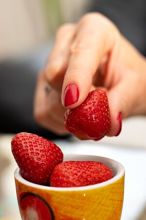 Woman hands with pretty red nail manicure, holding fresh ripe strawberries. Close up. Selective focus.の写真素材