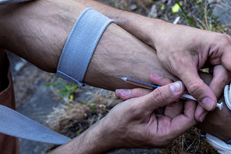 Hands of a drug addict with a syringe full of narcotic, heroin or cocaine to the leg veins. Drugs...