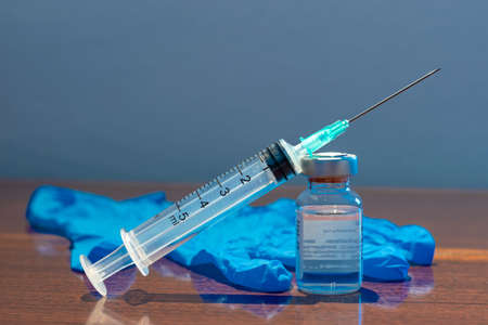 A bottle with vaccine and syringe with a needle in front of a blue surgical glove. Medicine, science and healthcare concept.の写真素材