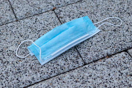 Improperly discarded blue medical face mask thrown away after use on the street footpath. COVID-19 waste or litter concept. Close up.の写真素材