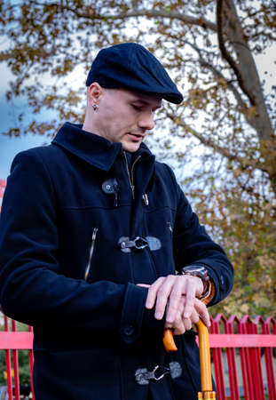 Portrait of a young man in black coat, standing on city streets waiting for a date and looking on...