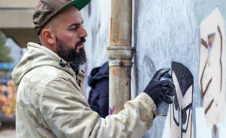 Street graffiti artist in action, drawing  with spray paint can on the wall in rainy weather. Street...