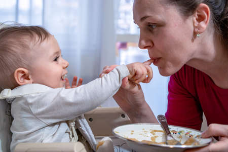 Happy and messy little baby and his mother feed each other. Healthy eating education since early days.の写真素材