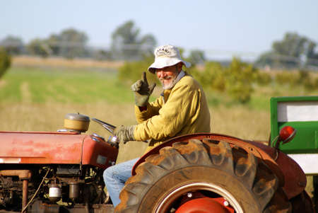 Happy farmer waving from his old red tracktor. Clearly he is very happy being a farmer.