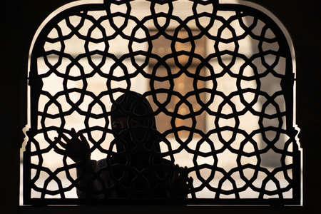 A Muslim girl in a black hijab stands behind a patterned wrought-iron fence. Woman in a conservative...