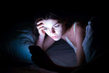 A woman with insomnia is watching a video online on a device.の写真素材