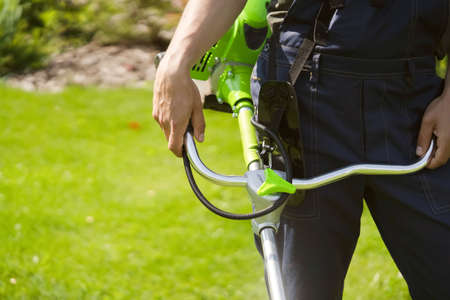 A close up of a white young man moving a lawn with a lawn mower in his hands