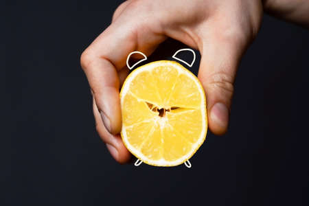 A mans hand holds a cut lemon, stylized as an alarm clock.