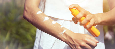 A young girl in a white dress applies sunscreen gel to her arms and shoulders.の写真素材