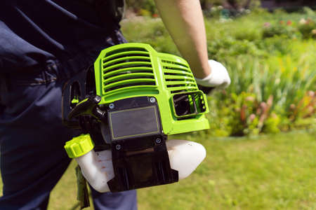 A close up of a white young man moving a lawn with a lawn mower in his hands