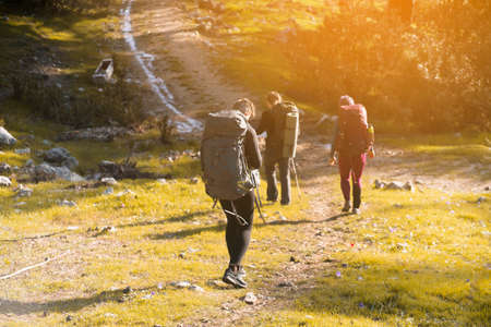 A group of young travelers are walking along a trail in the mountains at sunset.の写真素材