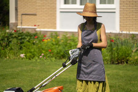 A girl is mowing a lawn in the backyard with an orange lawn mowerの写真素材