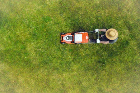 A young man is mowing a lawn with a lawn mower.の写真素材