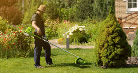 A young man with a lawnmower cares for the grass in the backyard.