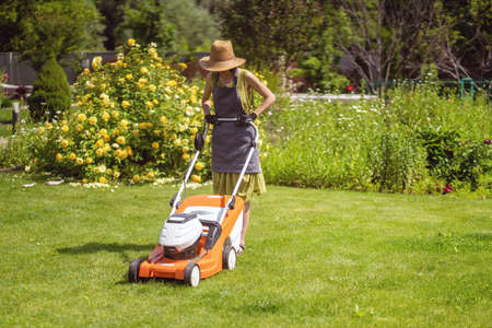 A young girl in a straw hat is mowing a lawnの写真素材