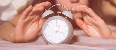 Hands of a young girl from under the blankets hold a retro vintage alarm clock