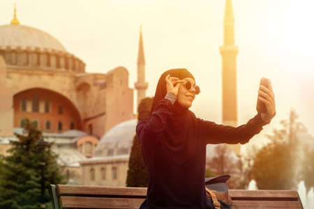 A young smiling Muslim girl in a hijab and stylish black glasses makes.の写真素材