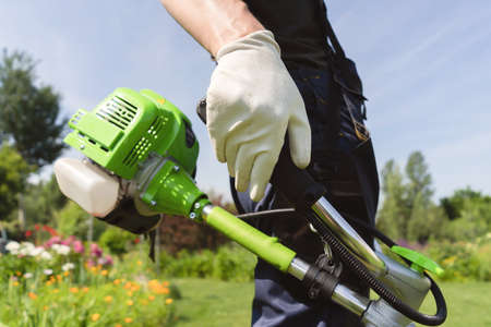 A close up of a white young man moving a lawn with a lawn mower in his handsの写真素材