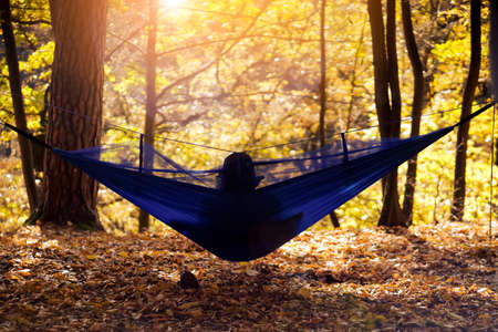 Traveler is sitting in a hammock in the sunny autumn day.の写真素材