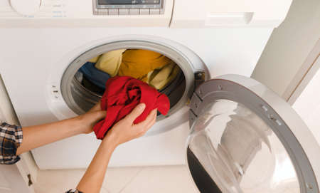 Woman puts bright clothes into a washing machine.の写真素材