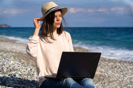 Girl in a hat works on a laptop on the beach, seashore.の写真素材