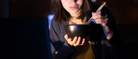 Girl eats noodles and watches video on a laptop.の写真素材