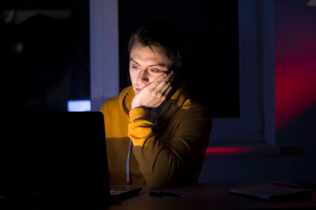 Man is working on a laptop at night at home.