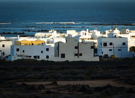 White buildings, town among volcanic black mountains and lava formations with an ocean on the...