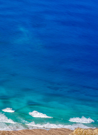 Blue ocean with waves and a sandy beach, top view.